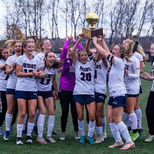 The Bangor Christian Patriots girls soccer team lifting the Maine state championship gold ball trophy on the field