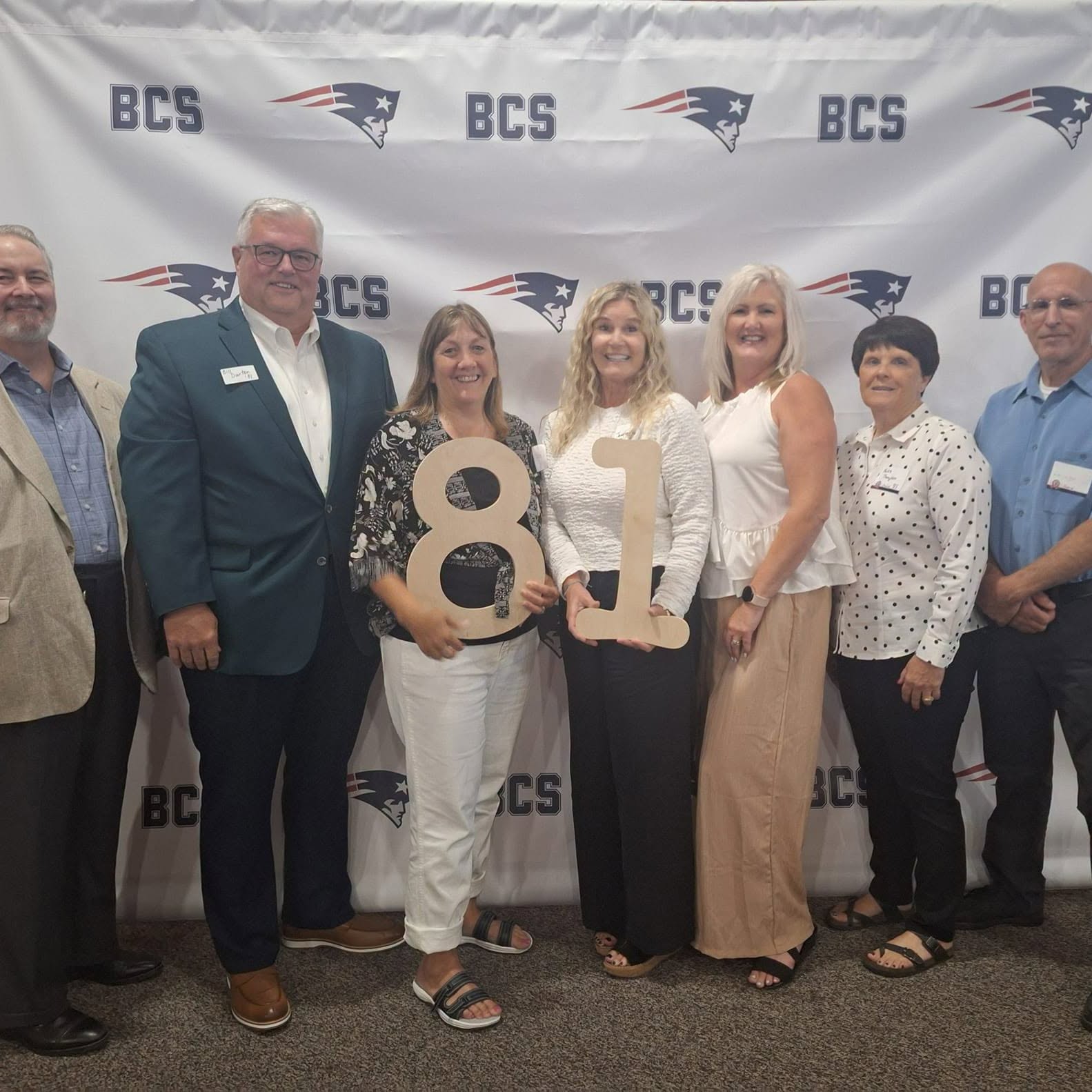 Alumni from the class of 1981 gathered at a reunion in front of a BCS Patriots backdrop