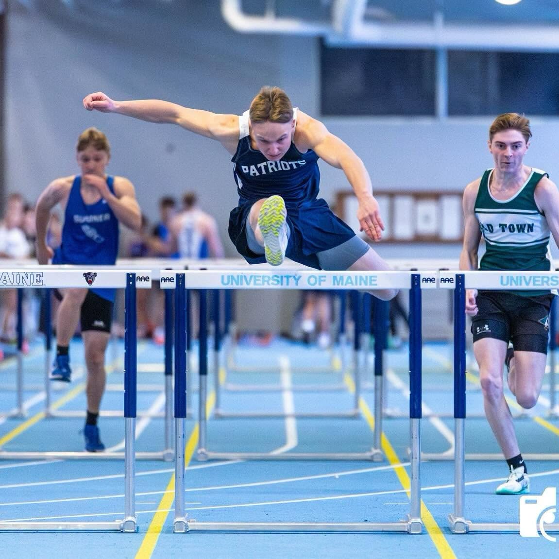 A Patriots hurdler clearing a hurdle at the University of Maine indoor track