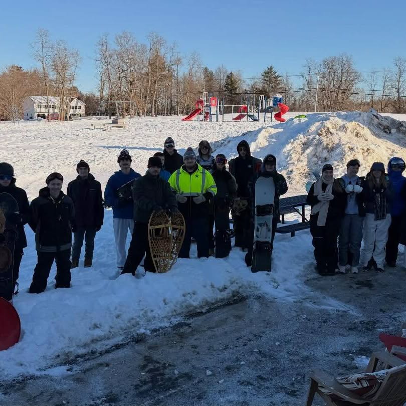 Students gathered outside in the snow with snowshoes and snowboards on a winter activity day