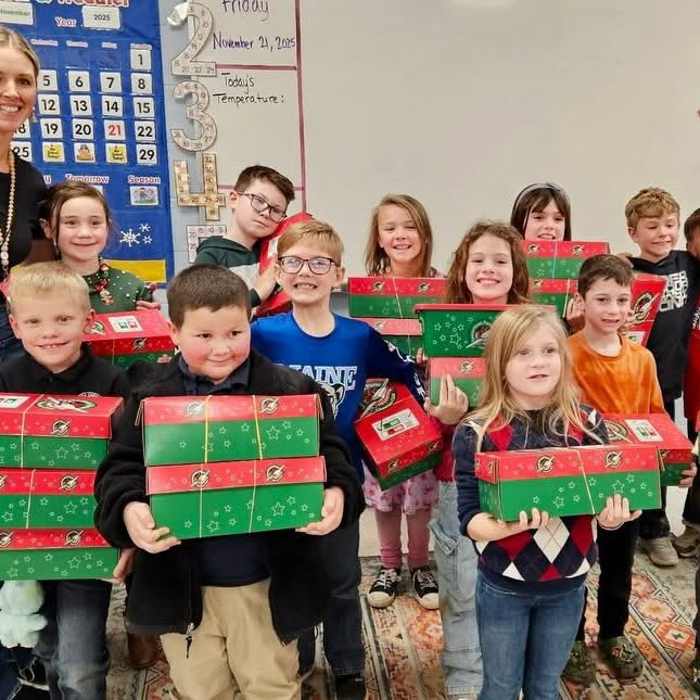 Elementary students holding Operation Christmas Child shoeboxes in their classroom